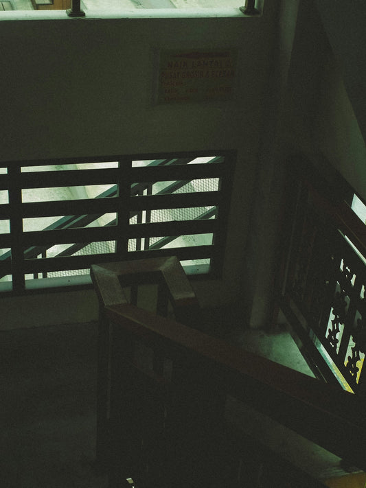 A dark staircase with wooden railings and a window.